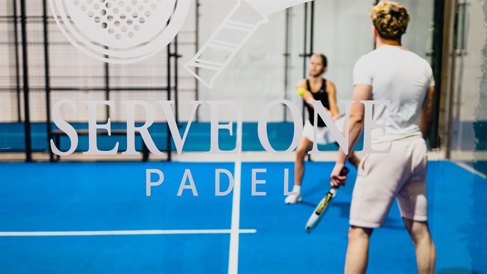 Zwei Spieler auf dem blauen Doppel-Court vor der Serve-One-Padel-Wand