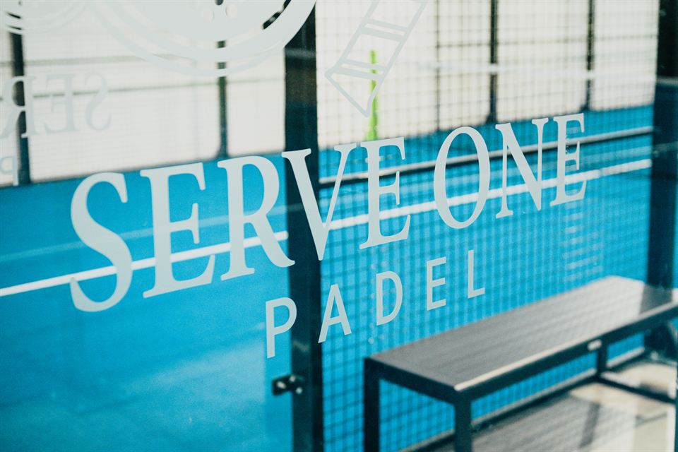 Wandschriftzug Serve One Padel neben einer Sitzbank in der Halle